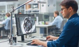 Over the Shoulder Shot of Engineer Working with CAD Software on Desktop Computer, Screen Shows Technical Details and Drawings. In the Background Engineering Facility Specialising on Industrial Design Over the Shoulder Shot of Engineer Working with CAD Software on Desktop Computer, Screen Shows Technical Details and Drawings. In the Background Engineering Facility Specialising on Industrial Design